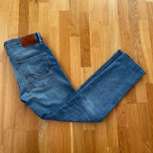 Blå jeans från Jack & Jones - Snygga blå jeans från Jack & Jones med klassisk femficksdesign och en bekväm passform. Perfekta för en avslappnad stil. Märkeslappen i läder ger en extra touch av stil. Lite mer av design jeans för j&j. Aldrig använda!
