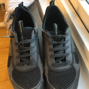 Svarta sneakers från EA7 Emporio Armani - Snygga svarta sneakers från EA7 Emporio Armani med meshdetaljer och snörning. Skorna har en diskret logga på sidan och en bekväm sula. Perfekta för en stilren look.