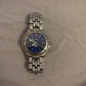 Silverfärgad klocka från Fossil - Snygg silverfärgad klocka från Fossil med blå urtavla och tydliga markeringar. Armbandet är i metall med en robust länkdesign och ett klassiskt spänne. Perfekt för den som gillar en stilren och tidlös look. Lite repig men värd priset.