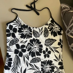 Svartvit blommig halterneck-topp - Snygg svartvit halterneck-topp med blommigt mönster. Perfekt för sommardagar med sitt lätta och luftiga material. Den har en knytning i nacken och en stilren design som passar till många olika outfits.