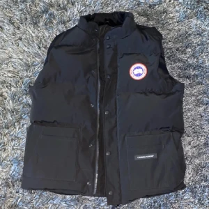 Canada Goose väst - Snygg svart dunväst från Canada Goose med knappar framtill och en hög krage. Den är använd två gånger. Det enda som är fel på västen är att en knapp inte går att knäppa. Förutom de så är den som ny. Nypris 6500. Skriv för prisförslag