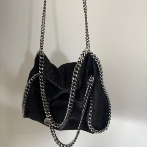 Stella McCartney  - Säljer min Stella McCartney Flabella Mini Tote Bag. Svart färg, silvriga detaljer. Väskan är köpt mars 2023 och är i gott skick. Dustbag, box och äkthetsbevis medföljer. Inköpspris: 9200kr, digitalt kvitto finns vid behov!