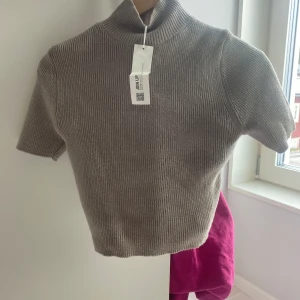 Beige ribbad polotröja - Säljer en stilren beige ribbad polotröja med korta ärmar. Perfekt för lager-på-lager eller som ett statement-plagg. Tröjan har en hög krage som ger en elegant touch. Passar både till jeans och kjol för en chic look.