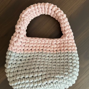 Handgjord stickad handväska i rosa och grått - Charmig handväska i en kombination av rosa och grått. Väskan är handgjord med ett stickat mönster och har ett robust handtag. Perfekt för att ge en unik touch till din stil.