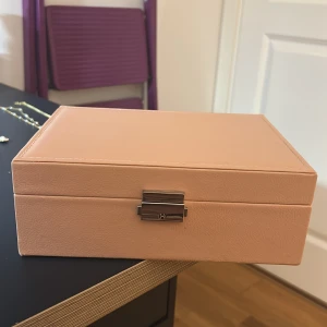 Smyckeskrin - säljer med allt i för 300kr - Ett elegant smyckeskrin i beige med flera fack för förvaring av smycken. Innehåller olika typer av smycken som halsband, armband och örhängen i olika färger och stilar. Perfekt för att organisera och skydda dina smycken.