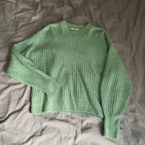 Grön stickad tröja från H&M - Säljer en mysig grön stickad tröja från H&M. Tröjan har en ribbad design och långa ärmar, perfekt för våren och sommaren!