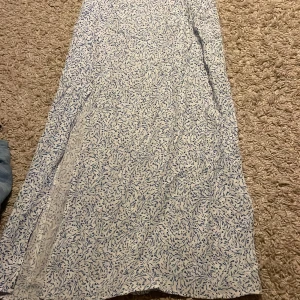 Vit och blå långkjol med blommönster - Säljer en vacker vit långkjol med blått blommönster. Kjolen har en luftig passform och är perfekt för varma dagar. Den är tillverkad i ett lätt material som ger en skön känsla. Perfekt för sommarens alla tillfällen! 🌸