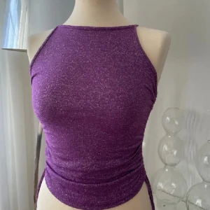 Lila glittrig linnetopp S/M - Snygg lila glittrig linnetopp med en tight passform. Perfekt för att lysa upp vilken outfit som helst. Toppen är ärmlös och har en stilren design.