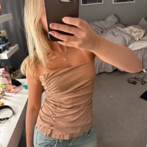 Rosa/ beige tubtopp - Säljer en snygg beige tubtopp med rynkade detaljer på sidan. Perfekt för en stilren och enkel look. Passar bra till jeans eller kjol. Rosa beige färg, använd fåtal gånger från Zara 