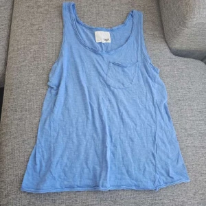 Blå linnetopp från 157 - Säljer en blå linnetopp från 157 med en liten bröstficka. Perfekt för varma dagar och enkel att matcha med andra plagg. Toppen har en avslappnad passform och är tillverkad i ett mjukt material. Ett litet hål finns i bak långt ner se bild 