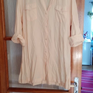 Aprikos långärmad skjorta stl L/Xl - Säljer en stilren Aprikos  långärmad skjorta med knappar framtill. Skjortan har en klassisk krage och två bröstfickor med lock. Perfekt för en avslappnad look.