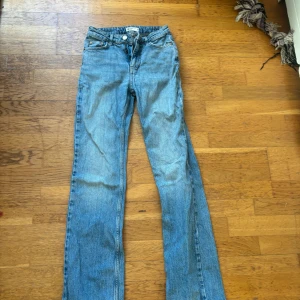 Blå jeans från Gina tricot  - Säljer ett par klassiska blå jeans från Gina Tricot. De har en rak passform och är tillverkade i slitstarkt denim. Jeansens design inkluderar en dragkedja och knappar framtill. 