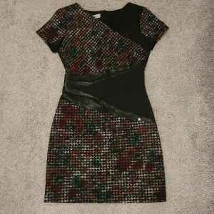 Mönstrad klänning med läderdetaljer - Snygg kortklänning med ett färgglatt rutigt mönster och svarta läderdetaljer. Perfekt för en classy look på jobbet, eller vardagligt. Endast använd en gång. 