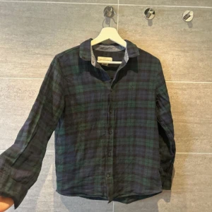 Rutig skjorta från L.O.G.G. - Snygg rutig skjorta i grönt och blått från L.O.G.G. med klassisk krage och knappar framtill. Perfekt för en avslappnad stil. Skjortan har långa ärmar och en liten broderad detalj på bröstet.