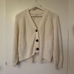 Vit stickad kofta från Lindex - Säljer en mysig vit stickad kofta från Lindex med stora knappar framtill. Koftan har en avslappnad passform. Den är i mycket bra skick, använd fåtal gånger. Storlek 146/152. 