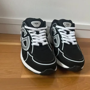 Svarta sneakers från D - Snygga svarta sneakers från D med vita och grå detaljer. Skorna har en robust sula och klassisk snörning. Perfekta för en stilren look.