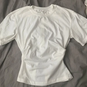 Vit t-shirt med öppen rygg - Säljer en stilren vit t-shirt med en unik öppen ryggdetalj. Perfekt för en avslappnad look med en twist.