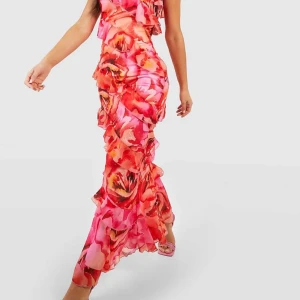 Färgglad långklänning med volanger - Säljer en färgglad långklänning med ett blommigt mönster i rosa och orange toner. Klänningen har en one-shoulder design med volanger som ger en romantisk känsla. Perfekt för sommarens fester! Oanvänd! Pris lapp kvar 