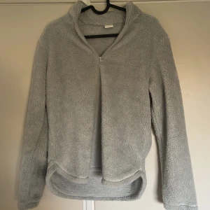 Grå fleece tröja med dragkedja - Mysig ljus blå fleece tröja med halv dragkedja och hög krage. Perfekt för kyliga dagar. Tröjan har en avslappnad passform och är supermjuk att ha på sig. Ett måste för höst- och vintergarderoben!