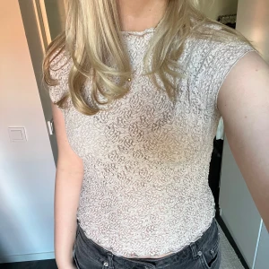 Beige spetsblus - Säljer en söt beige spetsblus med korta ärmar. Blusen har ett fint mönster och en lätt croppad passform. Perfekt för en stilren look.