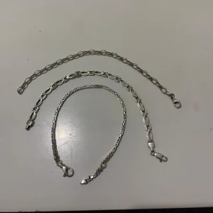 Tre silverfärgade armband - Säljer tre stilrena armband i silverfärg. Varje armband har en unik kedjedesign och är utrustade med karbinhake för enkel användning. Perfekta för att lägga till en elegant touch till din stil.