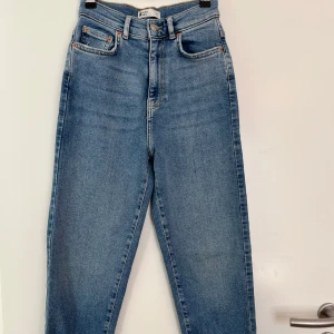 Blå jeans från Gina Tricot - Snygga blå jeans från Gina Tricot med hög midja och klassisk femficksdesign. De har en knapp och dragkedja framtill samt orange sömmar som ger en cool kontrast. Perfekta för en avslappnad stil.