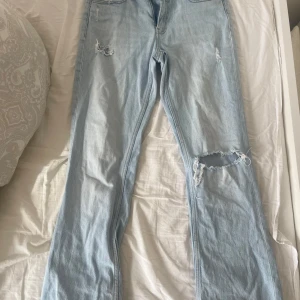 Ljusblå jeans med hål från Gina Tricot - Säljer ett par super guliiiigaljusblå jeans från Gina Tricot med slitna detaljer på benen!! De har en klassisk femficksdesign och är perfekta för en avslappnad stil. Passar bra till sneakers eller boots. Bootcut form från Gina Young. Passar tonåringar från ålder ca 11-13 år