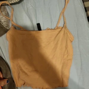 Beige linnetopp från H&M Divided - Säljer en stilren beige linnetopp från H&M Divided. Toppen har smala axelband och en enkel design som passar perfekt till sommaren. Perfekt för att matcha med jeans eller kjol för en avslappnad look.