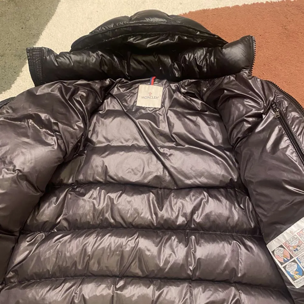 Säljer en snygg svart dunjacka från Moncler med huva och dragkedja. Jackan har en quiltad design och två fickor med dragkedjor. Perfekt för kalla dagar!. Takit.