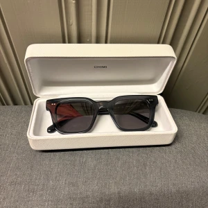 Svarta solglasögon från Chimi - Snygga svarta solglasögon från Chimi med en klassisk rektangulär form. De kommer i ett stilrent vitt fodral med Chimi-logga och en matchande påse för extra skydd. Perfekta för att ge din outfit en cool touch.