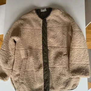 Beige teddyjacka med quiltad insida - Jättesnygg beige Neo Noir teddyjacka med en quiltad insida i olivgrön färg som också går att vända utåt. Den kan alltså användas åt båda hållen. Den har fickor och knappar. Perfekt för hösten och våren!