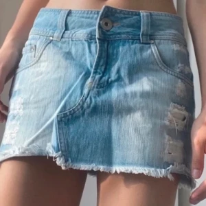Blå jeanskjol från Bershka - Säljer en snygg lowwaist blå jeanskjol  med slitna detaljer.  Den här jättefina fickor med stjärnor av diamanter på😍jättefint skick😇midjemått:36
