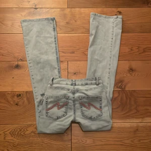 Ljusblå bootcut jeans med slitningar - Såå snygga  jeans från Nelly med rosa detaljer på bakfickorna och hål vid knäna. Använda 2 gånger. 