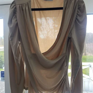 Beige långärmad topp från NA-KD - Säljer en elegant beige topp från NA-KD med långa ärmar och uringad framsida . Perfekt för en stilren look. Passar bra till både jeans och kjol.