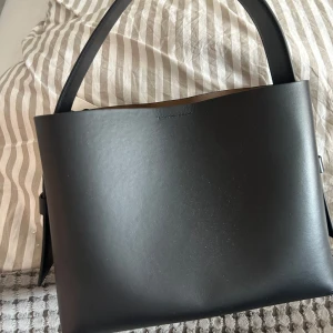 Svart handväska från Second Female - Elegant svart handväska i skinn från Second Female. Väskan har en stilren design med en praktisk dragkedja och ett rymligt inre. Perfekt till vardags. Nypris 4700kr