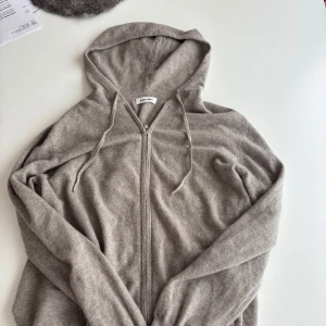 Grå hoodie i kashmir från Soft Goat - Mjuk och lyxig grå hoodie från Soft Goat i kashmir. Tröjan har dragkedja framtill, huva med snörning och långa ärmar. Perfekt för en avslappnad och stilren look. Pris 3000 kr, mitt pris 1500  kr. I princip helt oanvänd p.g.a att den är för stor. Tveka ej på att höra av er vid frågor eller funderingar 👊