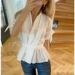 Zara vit omlottblus 🩷 - Säljer en fräsch vit omlottblus med volang nertill och knyt i midjan. Blusen har korta ärmar med knyt och en v-ringad omlottfront. Perfekt till jeans eller kjol för en stilren look. Passar S också 🩷