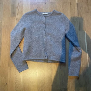 Grå kofta från Gina Tricot - Mysig grå kofta från Gina Tricot i mjukt material. Koftan har rund halsringning, långa ärmar och knäppning framtill med små knappar. Perfekt att slänga på sig över en topp eller t-shirt.