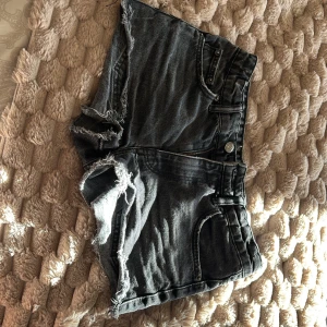 Svarta jeansshorts med fransar - Snygga svarta jeansshorts med råa franskantade benslut och klassisk femficksmodell. Shortsen har dragkedja och knapp framtill samt slitna detaljer för en cool look. Samt är de lågmidjade, säljer för att de är för små.