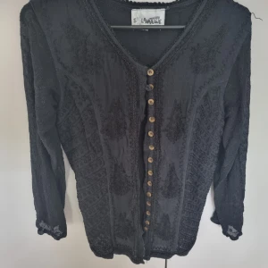 Fin Svart blus med spetsdetaljer storlek 36 - Fin blus som passar till både vardags och fest. Lite genomskinligt på ärmarna och fint mönster. Sitter tajt så väldigt fin!