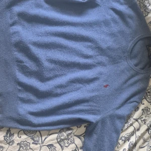 Blå merinoullströja från Polo Ralph Lauren - Säljer en klassisk blå tröja från Polo Ralph Lauren i 100% merinoull. Tröjan har rund halsringning, långa ärmar och den ikoniska lilla röda loggan broderad på bröstet. Perfekt för en stilren och bekväm look.