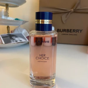 La Rive Her Choice Eau de Parfum - La Rive Her Choice är en parfym för kvinnor med en fräsch och blommig doftprofil. Flaskan är rektangulär i genomskinligt glas med ljusrosa vätska och blått lock med gulddetaljer. Doften har tydliga inslag av vita blommor, citrus, mysk, puder, vanilj, sötma och fräsch kryddighet.