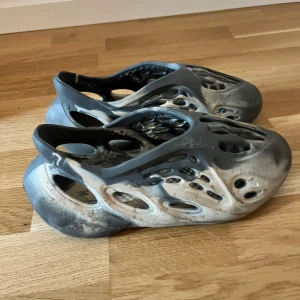Adidas Yeezy Foam Runner i svart och grå - Säljer ett par Adidas Yeezy Foam Runner i svart och grå marmorering. Skorna är tillverkade i syntetmaterial och har en futuristisk design med många hål för ventilation. Perfekta för dig som gillar streetwear och unika sneakers.