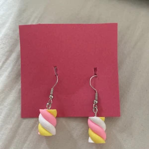 Färgglada örhängen med marshmallow-design - Säljer ett par unika örhängen som ser ut som små marshmallows i rosa, vitt och gult. Perfekta för dig som vill sticka ut med ett lekfullt och färgglatt smycke! Hängande modell med metallkrok.