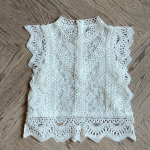 Vit spetstopp  - Superfin vit kort blus i spets Blusen har ett romantiskt mönster och är ärmlös, perfekt för att skapa en söt och trendig look. Köpt i London som present, aldrig andvänd skulle säga att den passar S/XS 💕(Pris kan diskuteras vid snabb affär)