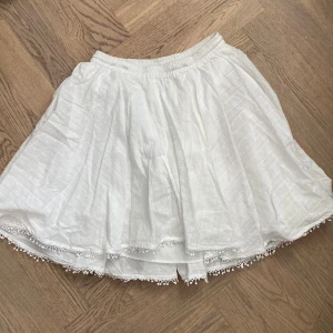 Vit kjol från Zadig & Voltaire - Säljer en vit kjol från Zadig & Voltaire i storlek 16 år (S i dam ungefär). Kjolen har elastisk midja och är dekorerad med små spetsdetaljer längs fållen. Den är luftig och har en lätt volangig form, perfekt för varma dagar. Helt nyskick då den köptes för ett specifikt tillfälle och aldrig andvöndes efter det💕Säljer även den tillhörande blusen om någon är Inter för ett set!