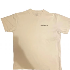 T-shirt från Polar Skate Co - Säljer en beige t-shirt från Polar Skate Co med liten logga på bröstet och coolt tryck på ryggen med text och illustration. Perfekt för dig som gillar streetwear och skate. Är 184 o passar bra