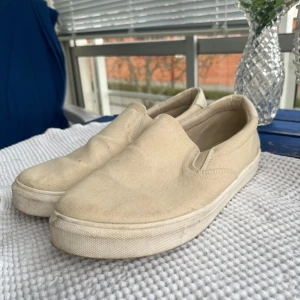 Beige slip-on sneakers från Linear of Sweden - Säljer ett par stilrena beige slip-on sneakers från Linear of Sweden. Skorna har en platt vit sula och är tillverkade i canvasmaterial. Perfekta för en avslappnad och enkel look.
