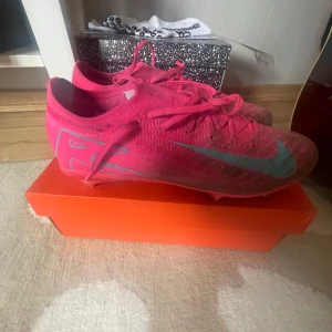 Nike fotbollsskor i rosa och turkos - Säljer ett par Nike fotbollsskor i en riktigt snygg rosa färg med turkosa detaljer och sula. Perfekta för dig som vill sticka ut på fotbollsplanen. Skorna har gått upp lite vid en dobb men annars är det i bra skick.