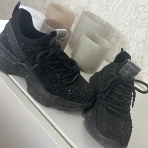 Svarta sneakers med glittriga detaljer - Säljer ett par svarta chunky sneakers med glittriga stenar över hela skon. Skorna har tjock sula, snörning och en sportig look. Perfekta för dig som vill sticka ut lite extra i vardagen. 